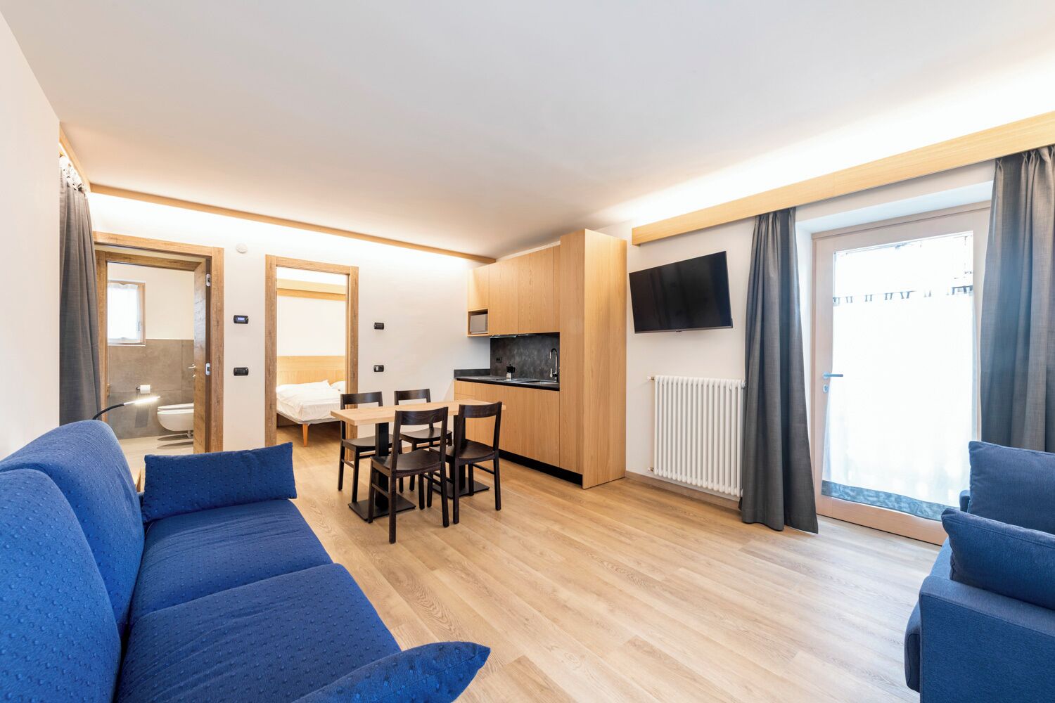 A compact living space with a kitchenette, a dining area, a sofa, and a TV mounted on the wall.