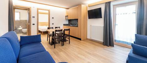 A compact living space with a kitchenette, a dining area, a sofa, and a TV mounted on the wall.