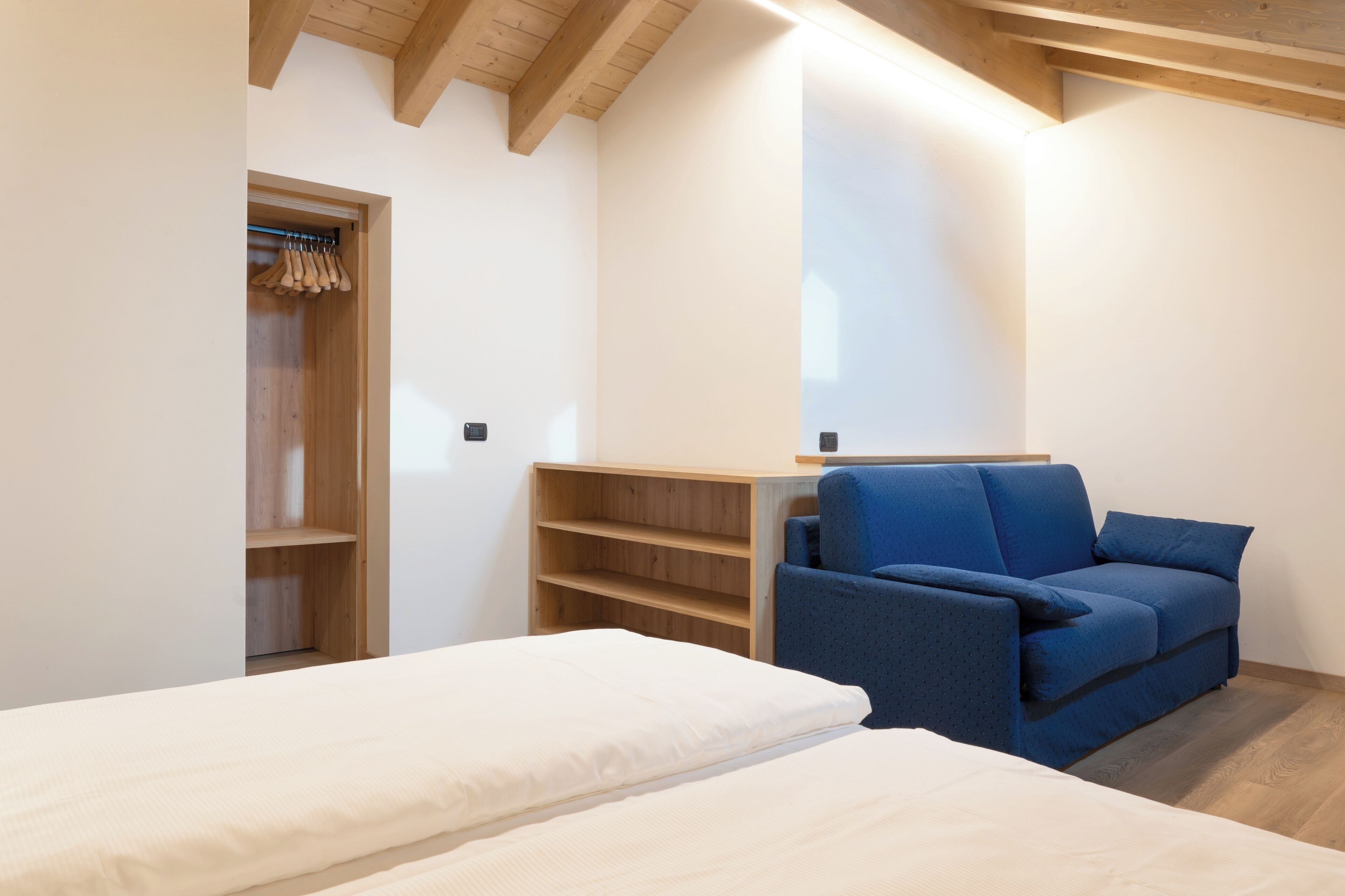 Un dormitorio moderno con techo de madera, un sofá azul y una cama blanca.