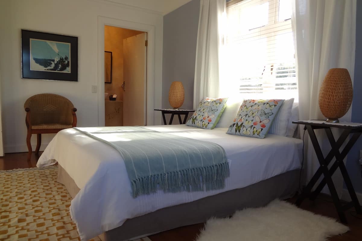 Quarto com cama, cadeira, tapete e tapete branco fofo, uma imagem na parede e uma janela com cortinas.