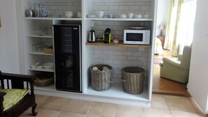 A kitchen with a black refrigerator, microwave, and shelves with kitchenware. There are wicker baskets and a wooden cabinet above the sink. - Walker Bay Manor (Hermanus)