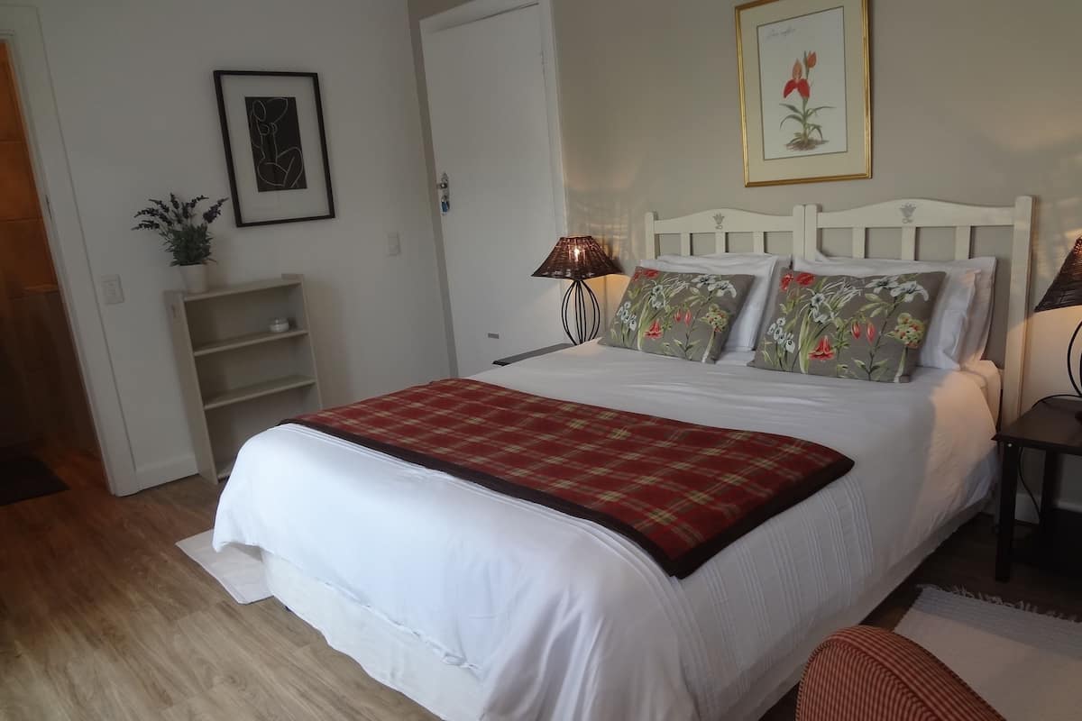 Quarto bem arrumado com uma cama grande, mesa de cabeceira, luminária e um quadro na parede.