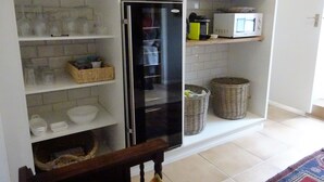 A kitchen with white cabinets, a black refrigerator, and shelves with dishes and kitchenware. - Walker Bay Manor (Hermanus)
