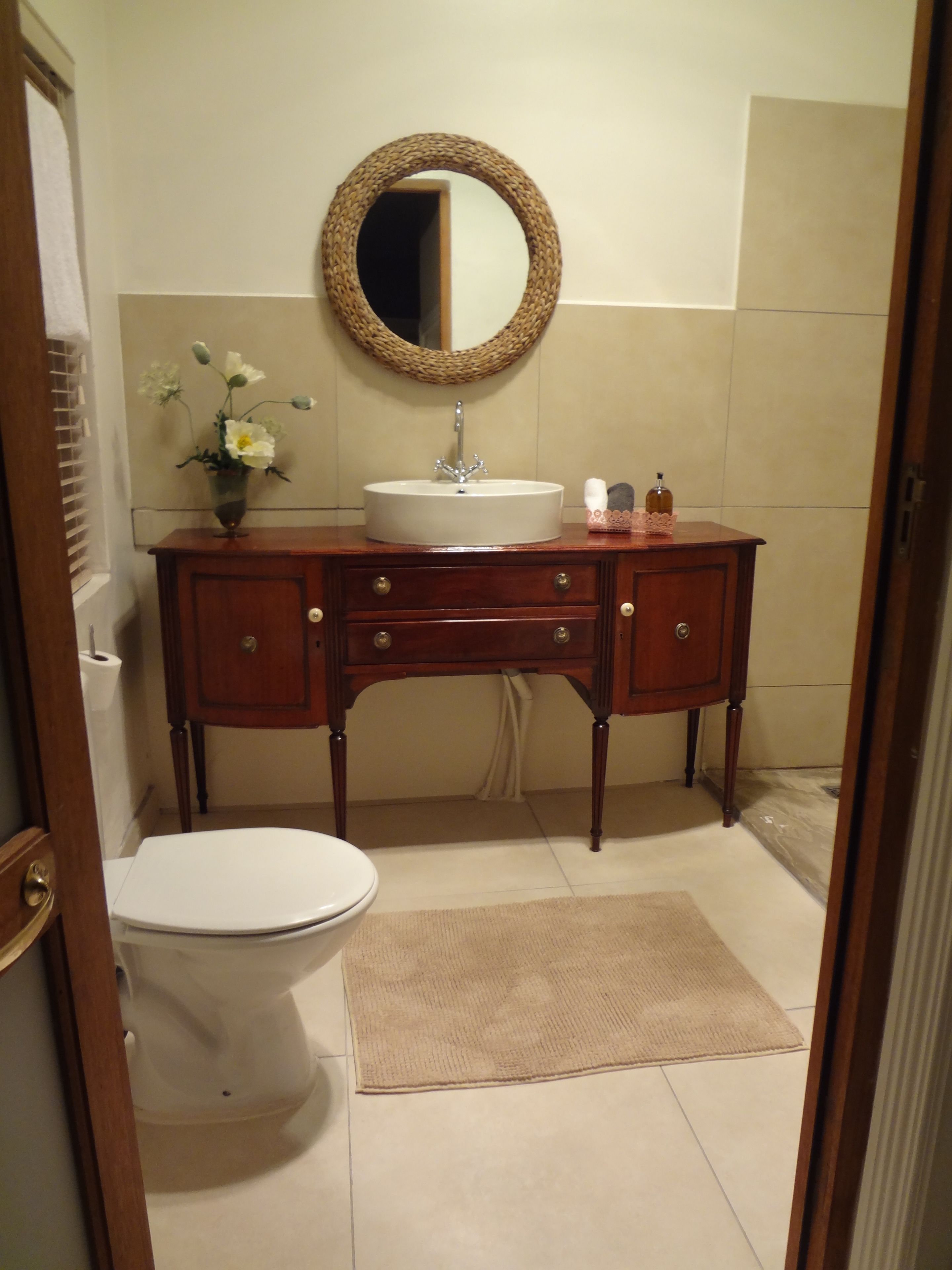 Un bagno con un mobile vanitario in legno, uno specchio rotondo, un lavandino bianco e un water.