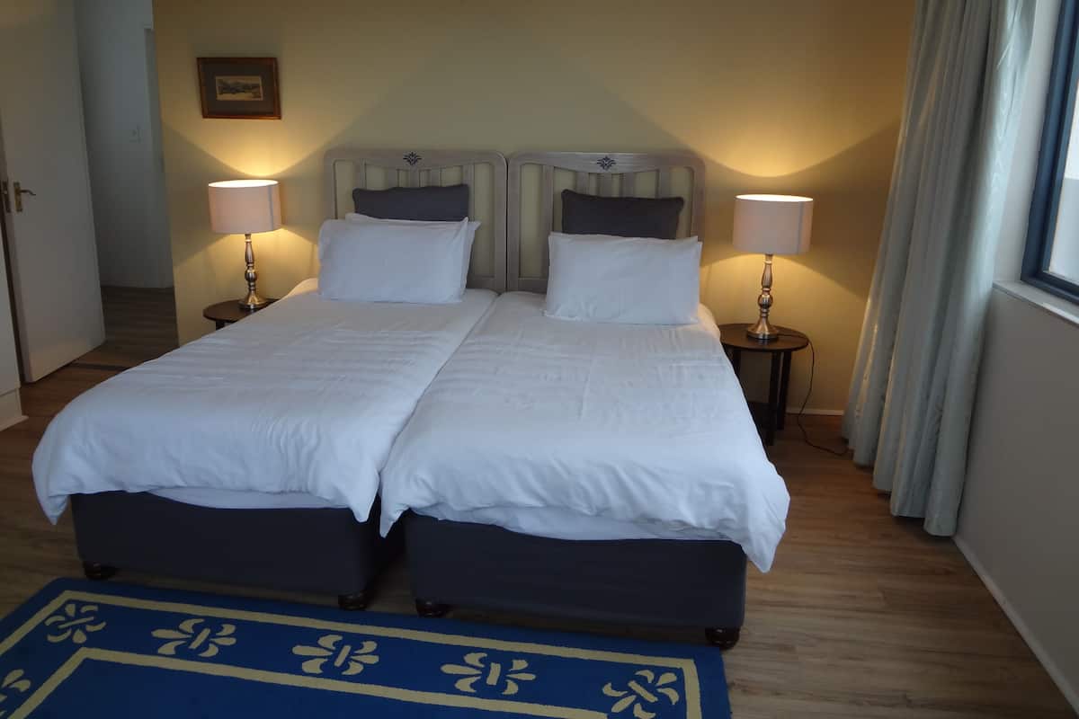 Uma cama de casal com duas mesas de cabeceira, cada uma com uma luminária, em quarto de hotel com piso de madeira e tapete azul.
