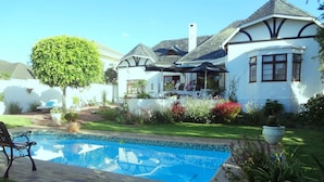 A pool with a tiled edge, surrounded by a garden with various plants and flowers. - Walker Bay Manor (Hermanus)