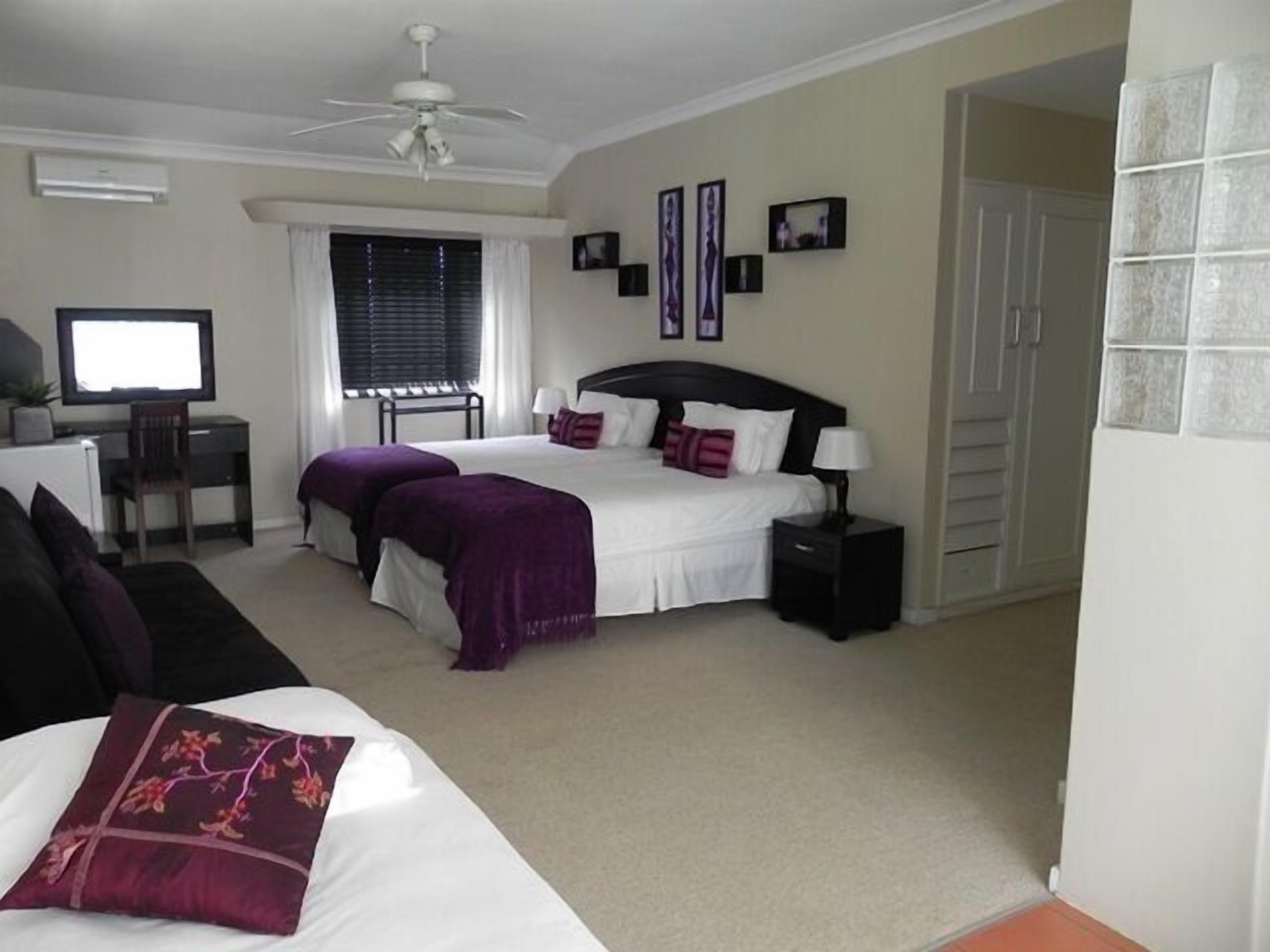 A bedroom with a bed, bedside tables, a desk, a chair, a television, and a ceiling fan.