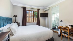 Una camera d'albergo con un letto, una scrivania con una sedia, una televisione e una finestra con tende.
