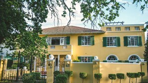 Un edificio giallo con persiane verdi, un cancello e un piccolo giardino con siepi curate.