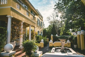 Een binnentuin met een fontein, plantenpotten en een geel gebouw met kolommen en luiken.