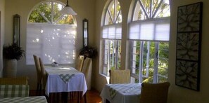 A dining area with a table set for two, surrounded by chairs, large windows with blinds, and framed artwork on the wall. - 268 On Ridge Guesthouse (Durban)