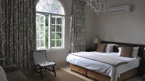 Quarto com uma cama grande, uma cadeira, uma janela com cortinas e um ar condicionado.