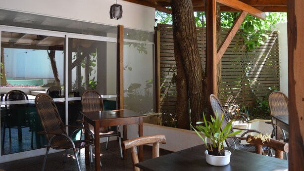 An outdoor patio area with wooden furniture, a table with a potted plant, and a view of a pool through a glass partition. - Kelta Hotel Puerto Iguazú Centro (Puerto Iguazú)