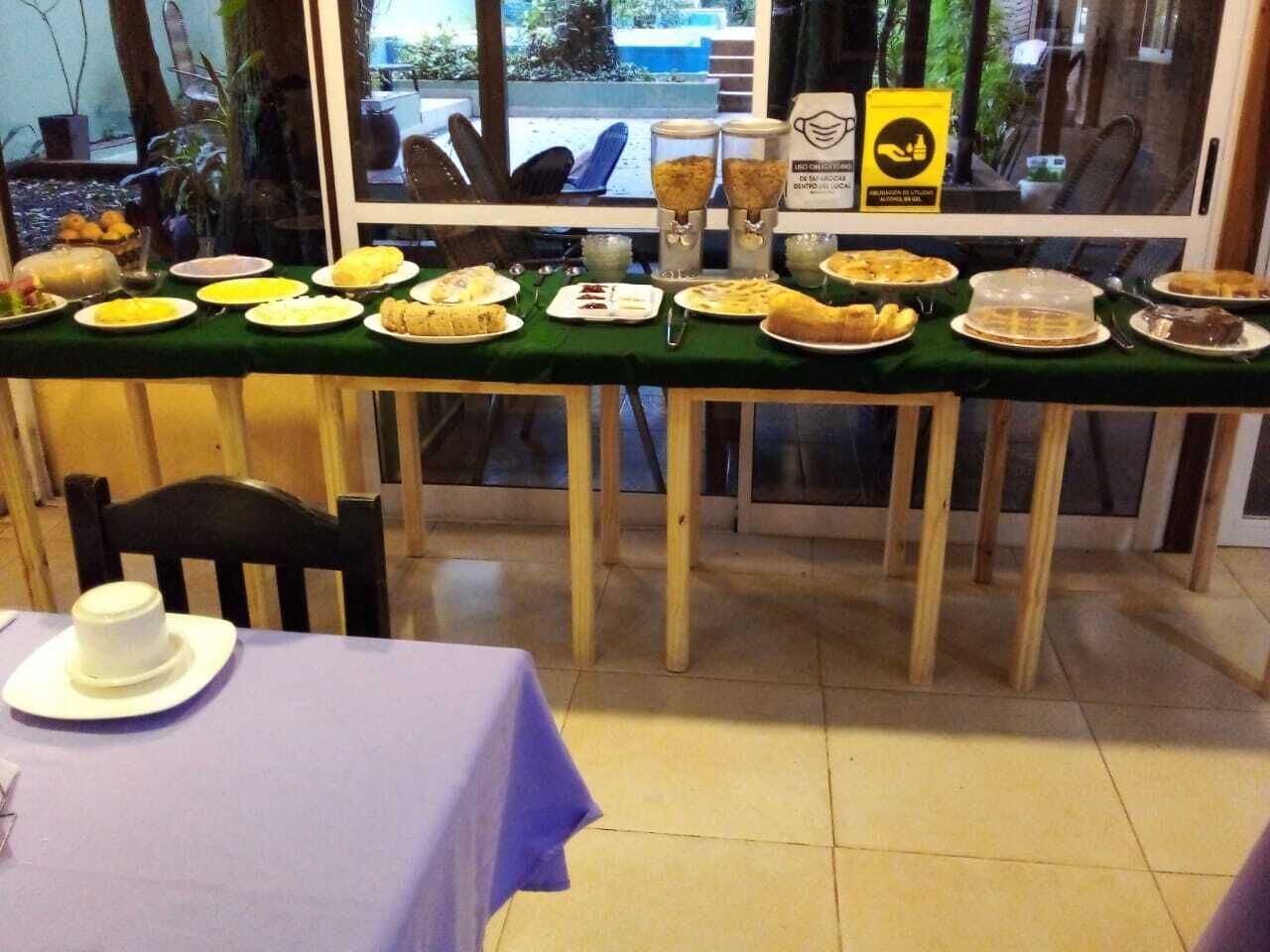 Un espace repas avec une longue table recouverte d’une nappe verte, différents plats et un panneau jaune orné d’un symbole représentant une main.