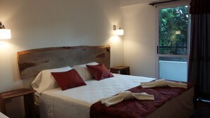 A hotel room with a large bed, two bedside tables, a wooden headboard, and a window with a view of greenery. - Kelta Hotel Puerto Iguazú Centro (Puerto Iguazú)