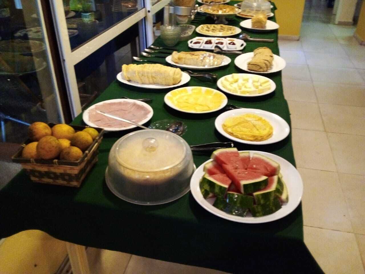 A buffet table with various dishes including fruits, desserts, and a covered container.