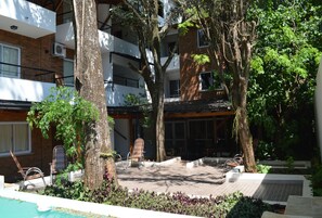 A courtyard with a pool, lounge chairs, and a covered seating area surrounded by trees and plants. - Kelta Hotel Puerto Iguazú Centro (Puerto Iguazú)