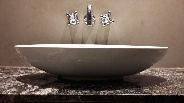 Un lavabo ovalado grande y blanco con dos grifos de cromo sobre una encimera de granito.