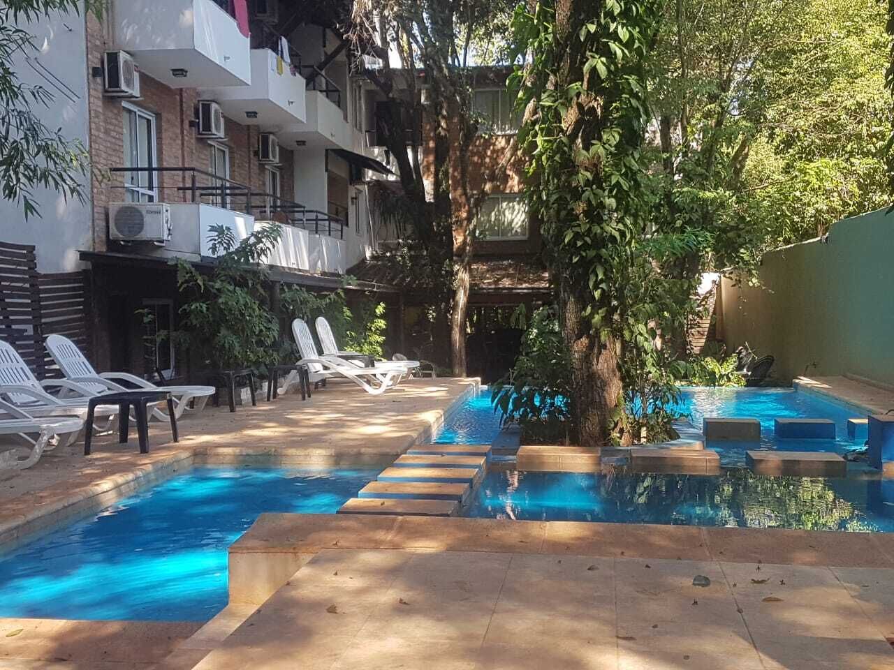 A swimming pool with steps leading into it, surrounded by lounge chairs and a tree.