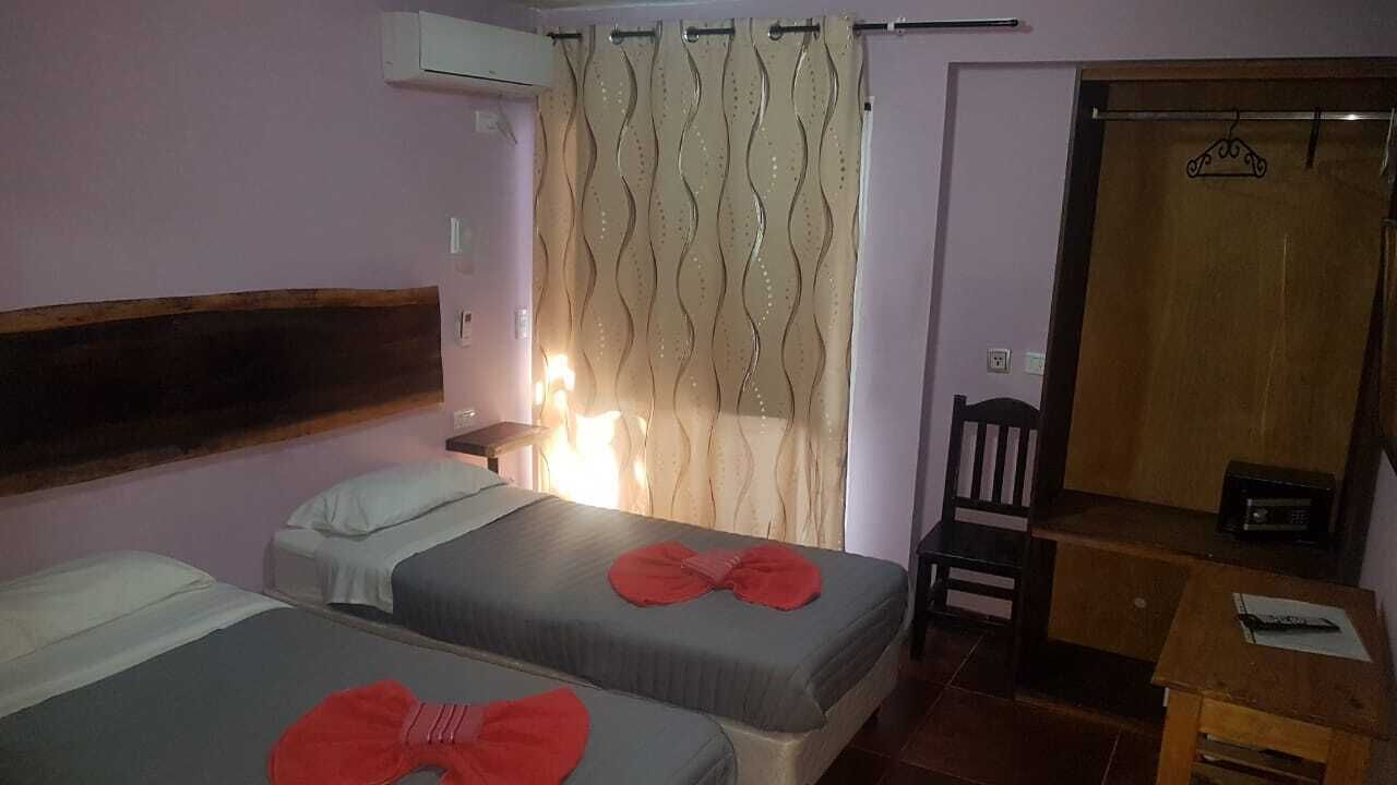 A room with two beds, a wooden headboard, a small table, a chair, and a curtain.
