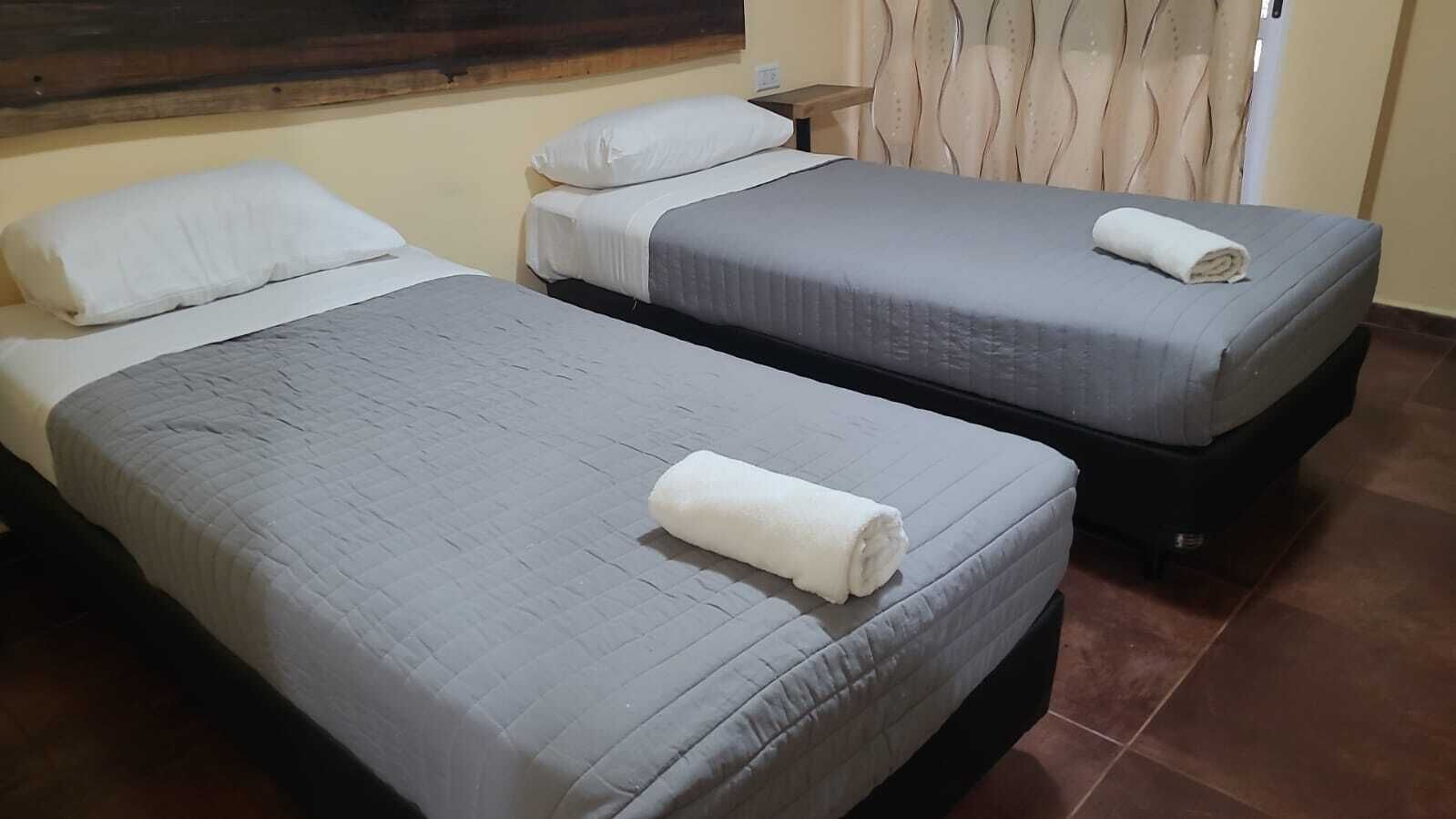 Une chambre d’hôtel avec deux lits simples, chacun recouvert d’une couverture grise et agrémenté d’oreillers blancs.
