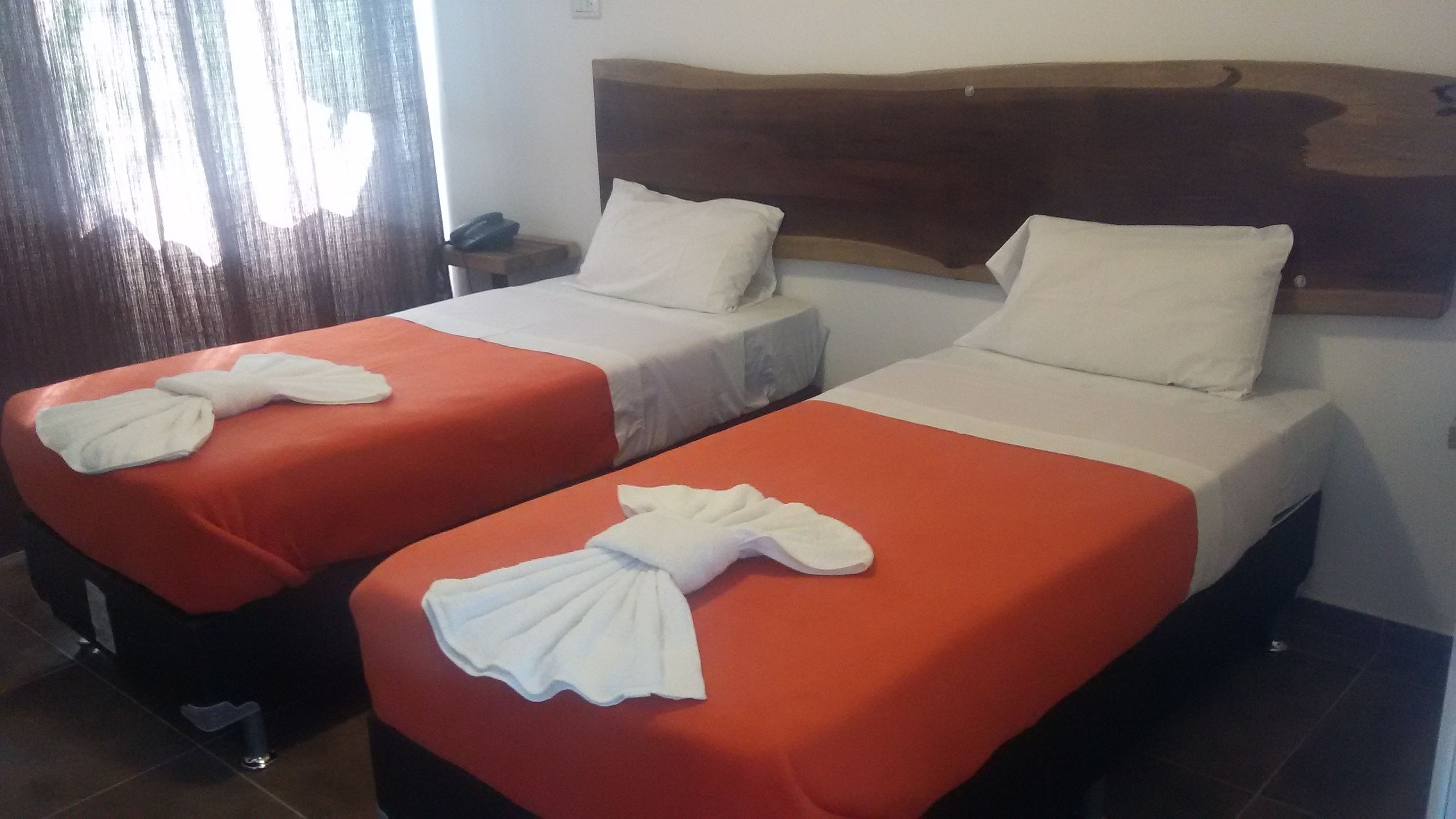 Deux lits simples avec des oreillers blancs et des couvre-lits orange, une tête de lit en bois et une petite table de chevet avec un téléphone.