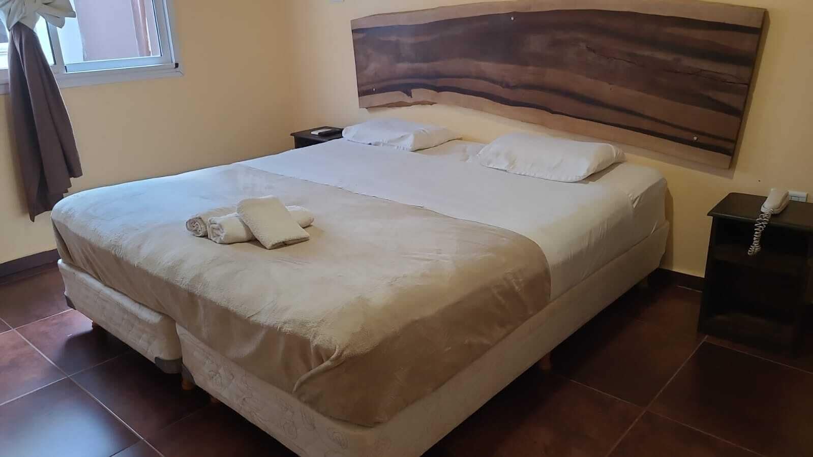 Een groot bed met hoofdeinde, nachtkastje en telefoon ernaast.