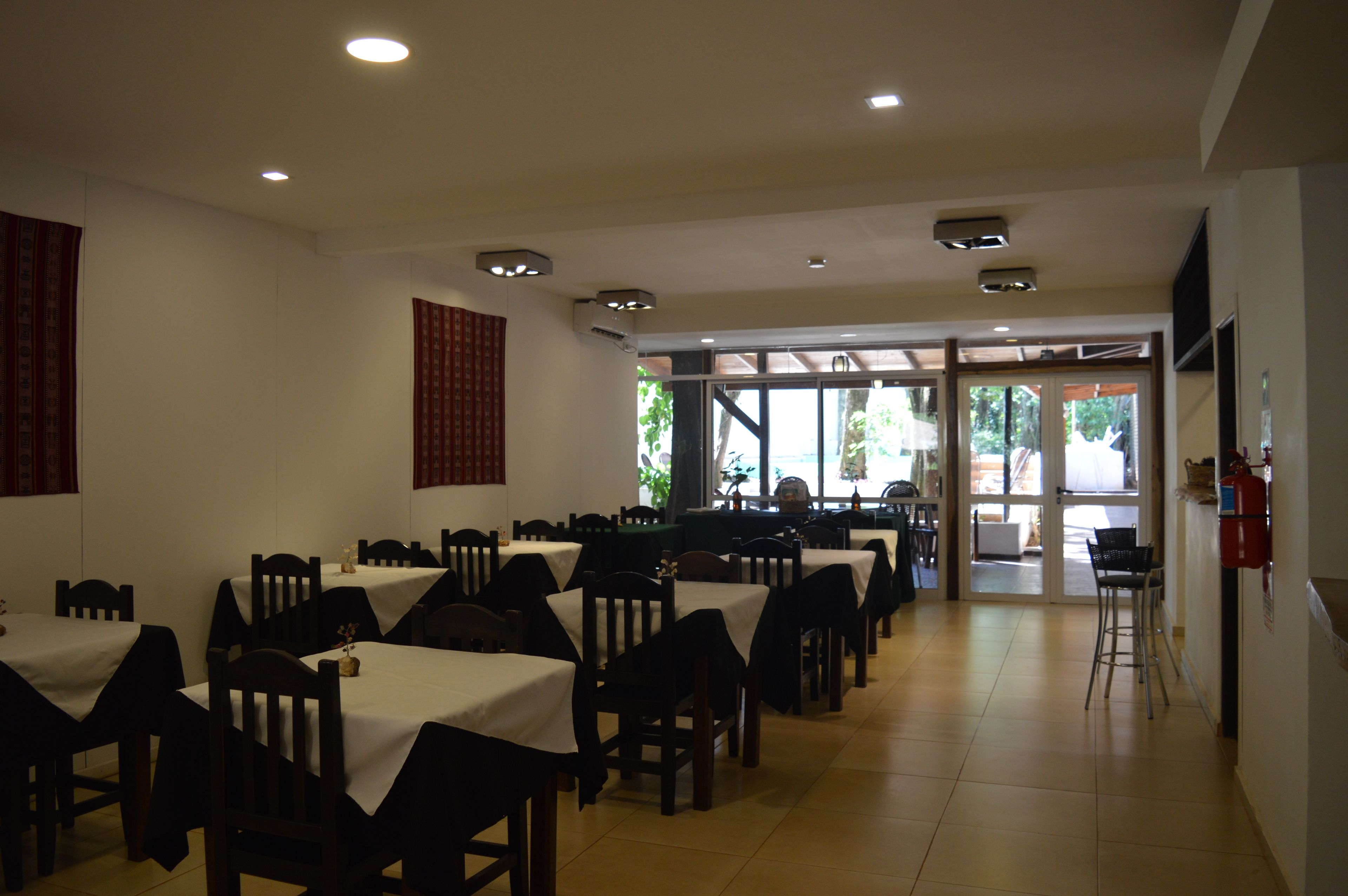 Un espace repas avec des tables et des chaises, un extincteur et une vue sur l’extérieur.