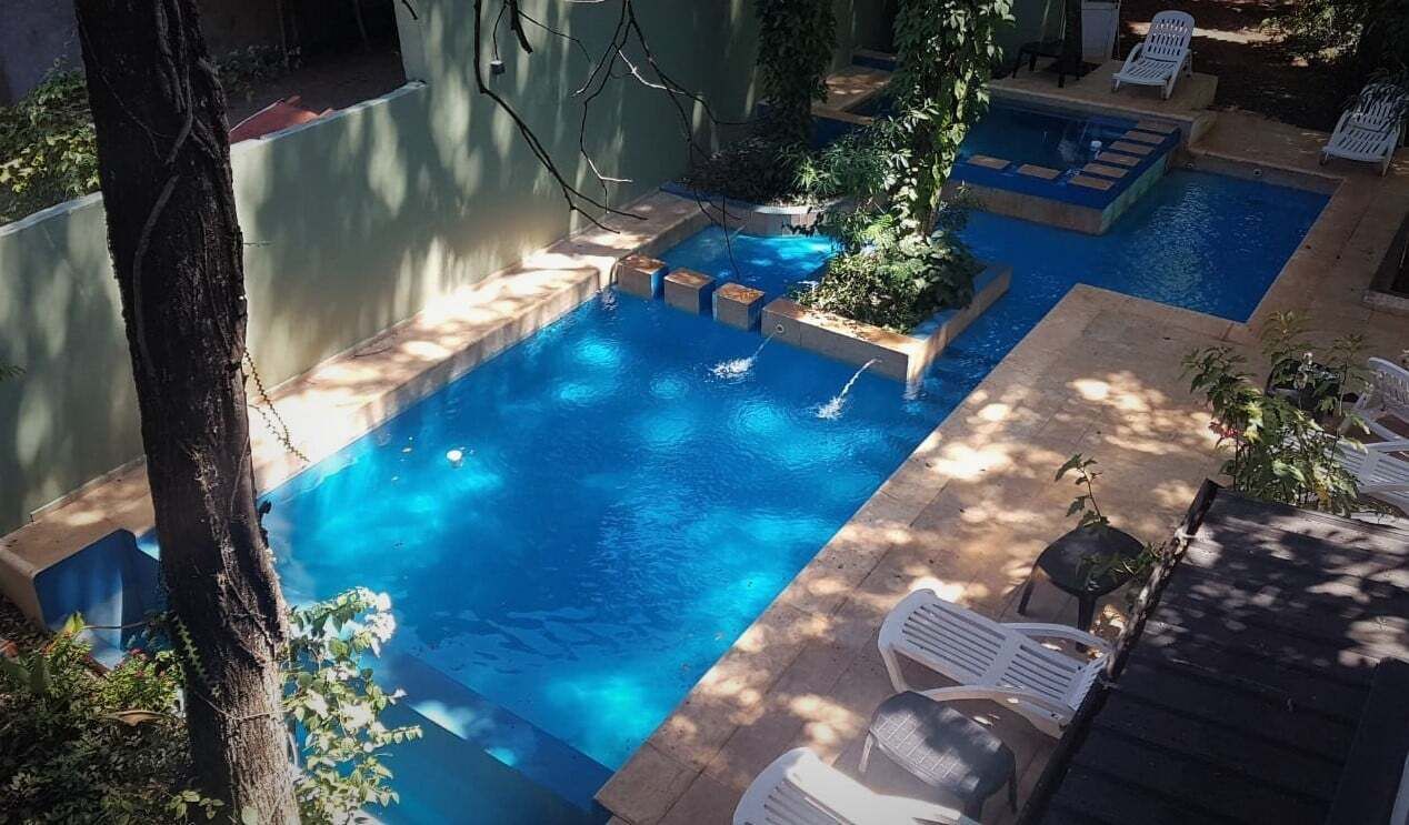 Una piscina con varias secciones, rodeada de sillas de descanso y plantas en macetas.