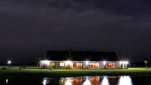 A large, modern building with multiple illuminated windows and a reflective water body in front. - Otterskloof Private Game Reserve (Kopanong)