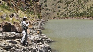 A person fishing by a calm river with rocky banks and sparse vegetation. - Otterskloof Private Game Reserve (Kopanong)