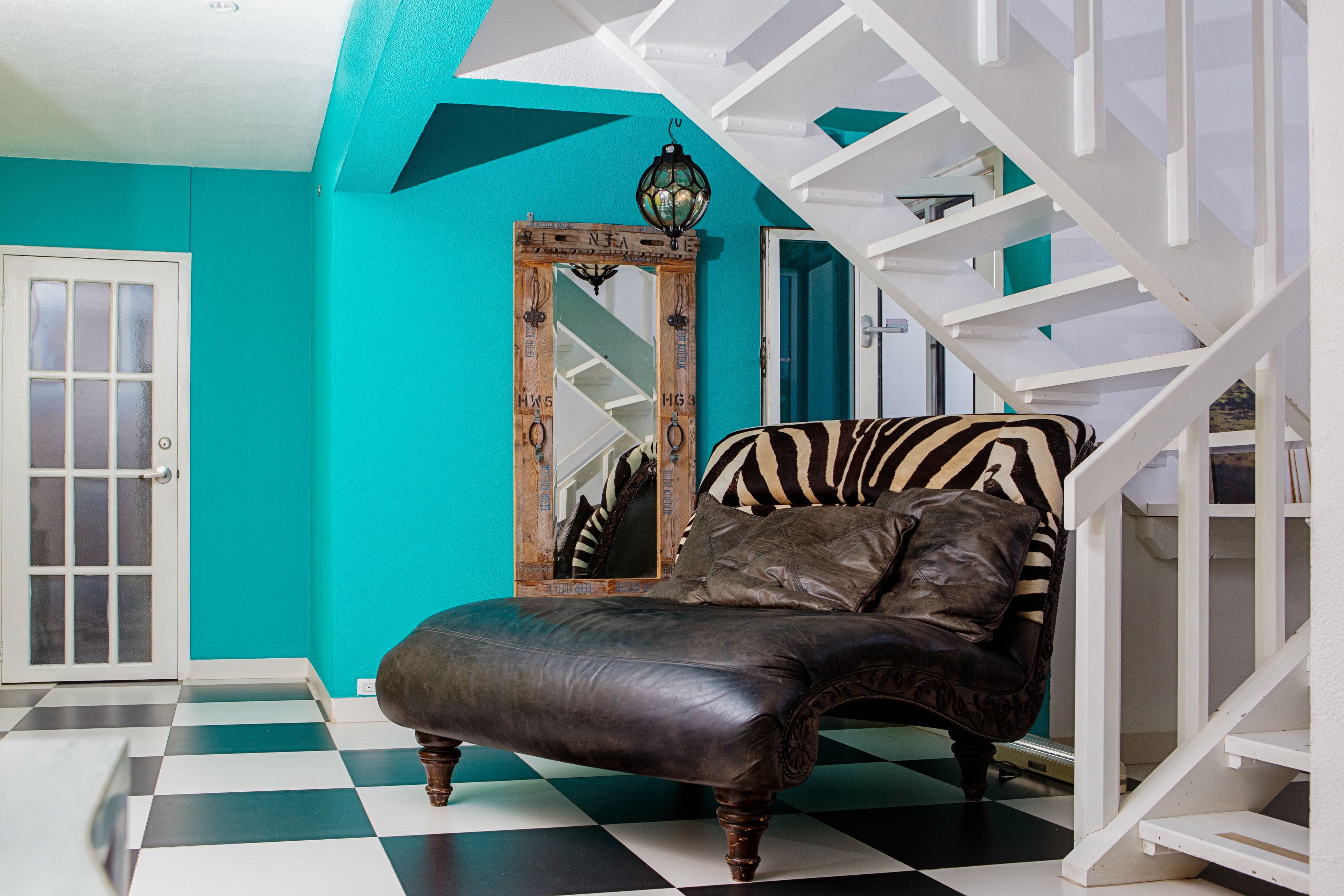 A room with a checkered floor, a zebra-patterned sofa, a wooden-framed mirror, and a staircase with white railings.