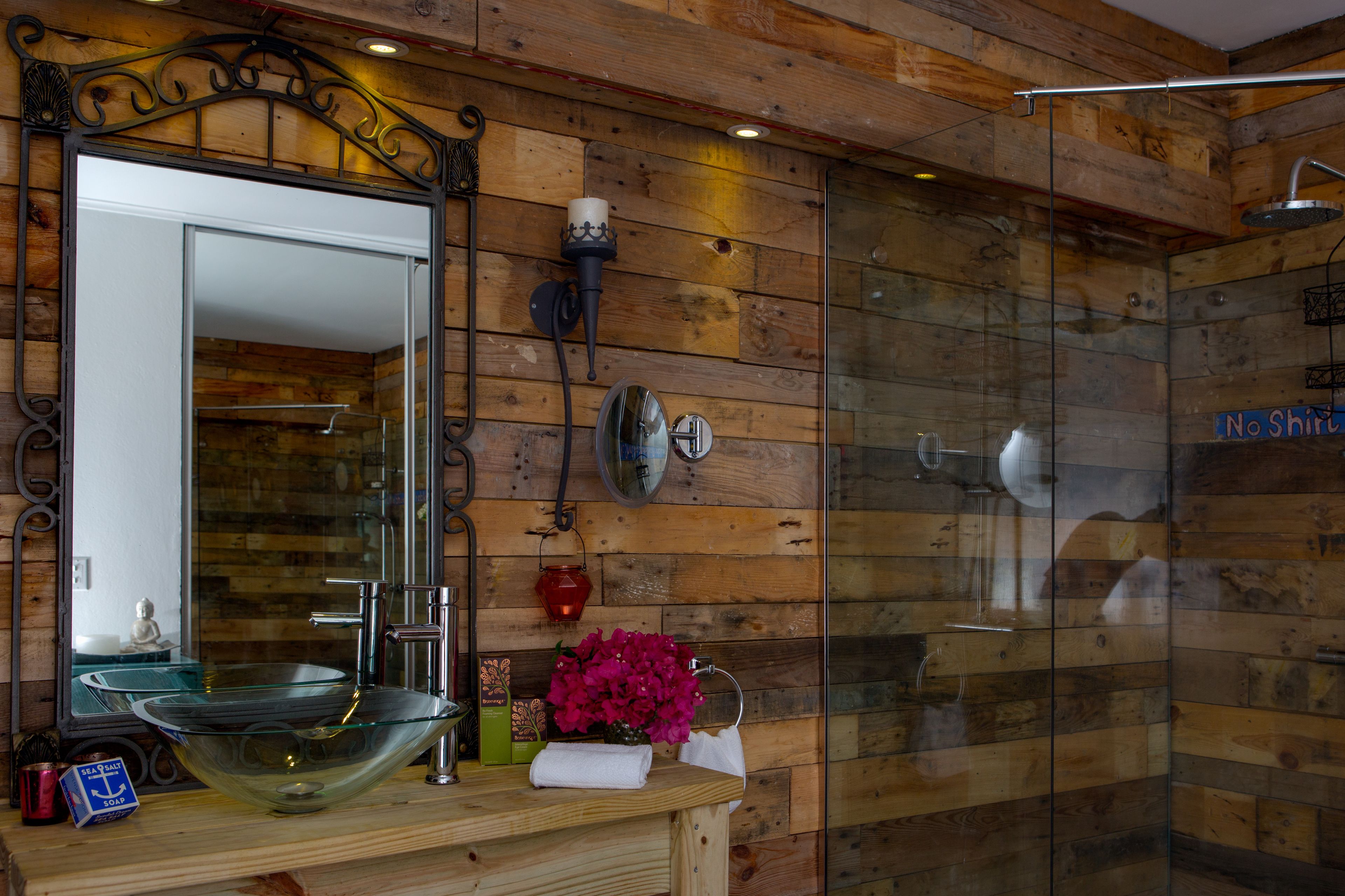 A bathroom with a wooden wall, a glass shower enclosure, a large mirror, and a glass bowl sink.