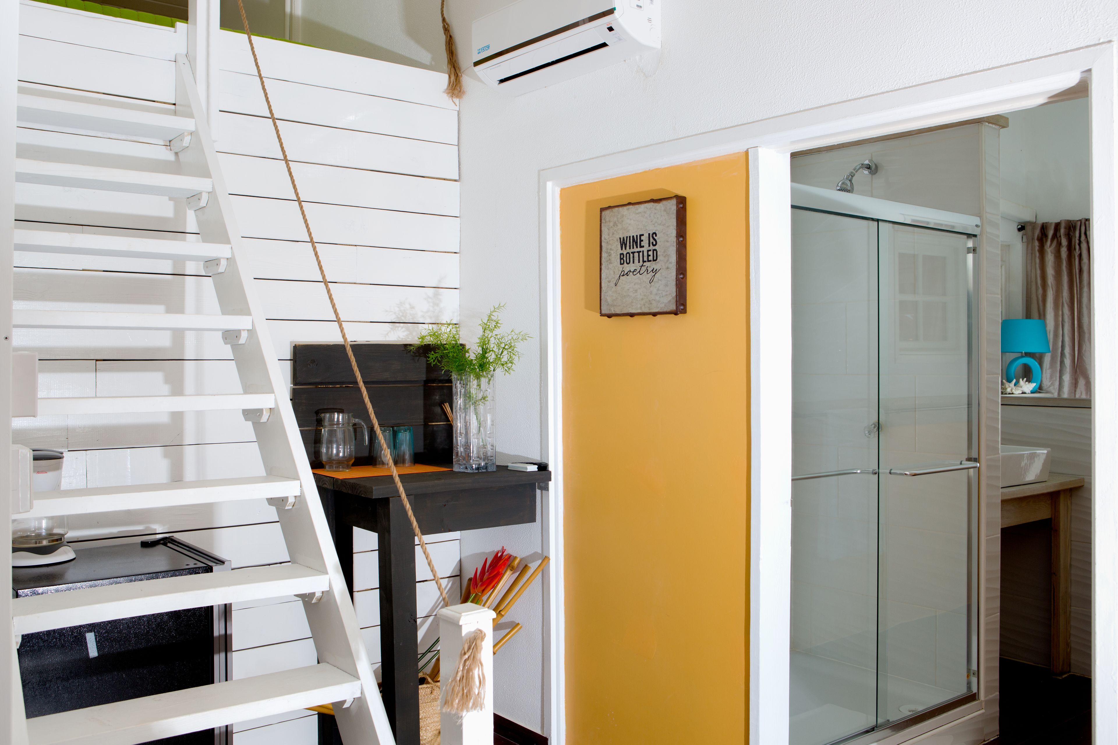 A staircase with a white railing, a black table with a vase and a plant, and a yellow wall with a framed quote.