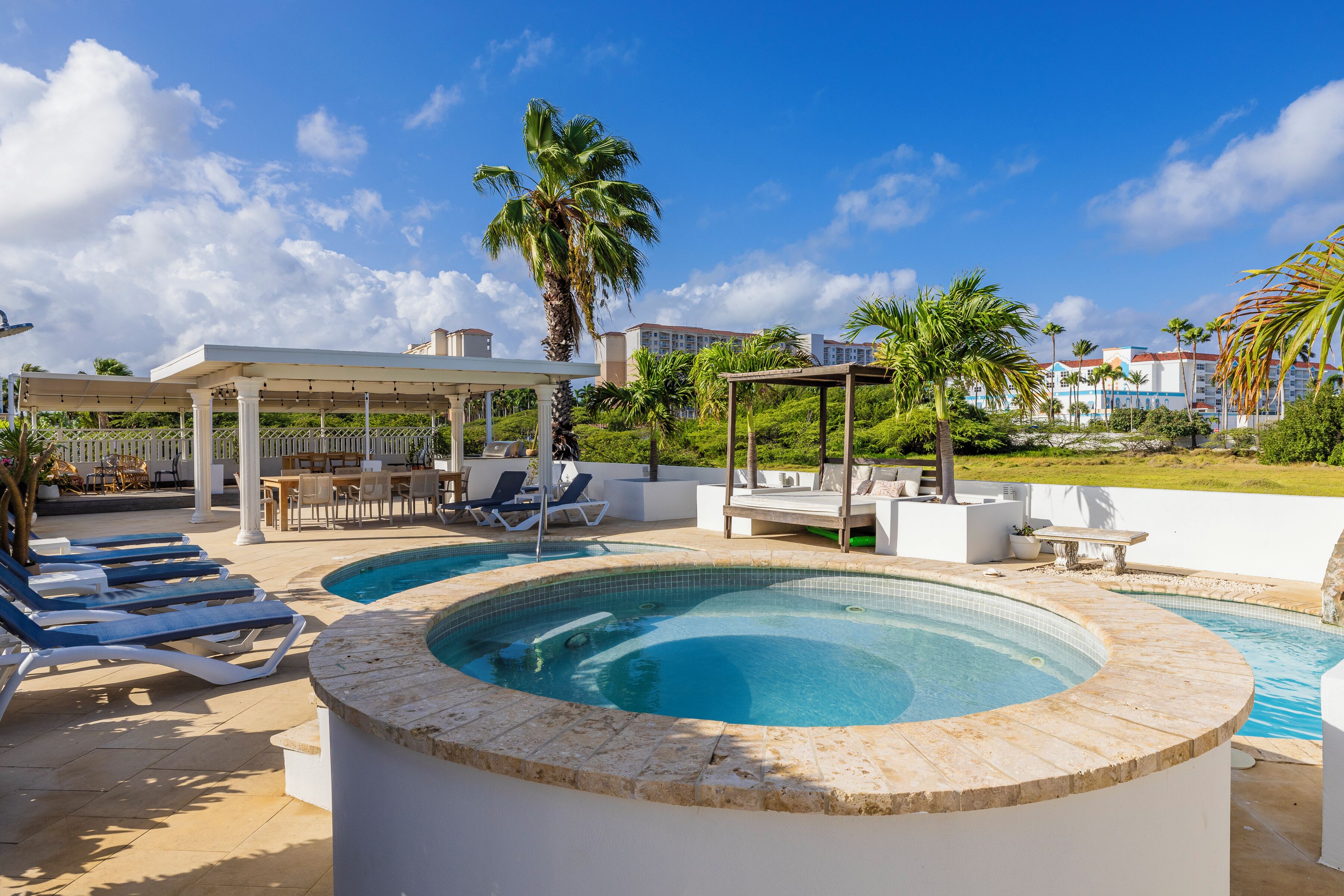 Zona de piscina con sillones reclinables, jacuzzi y un área de estar techada.
