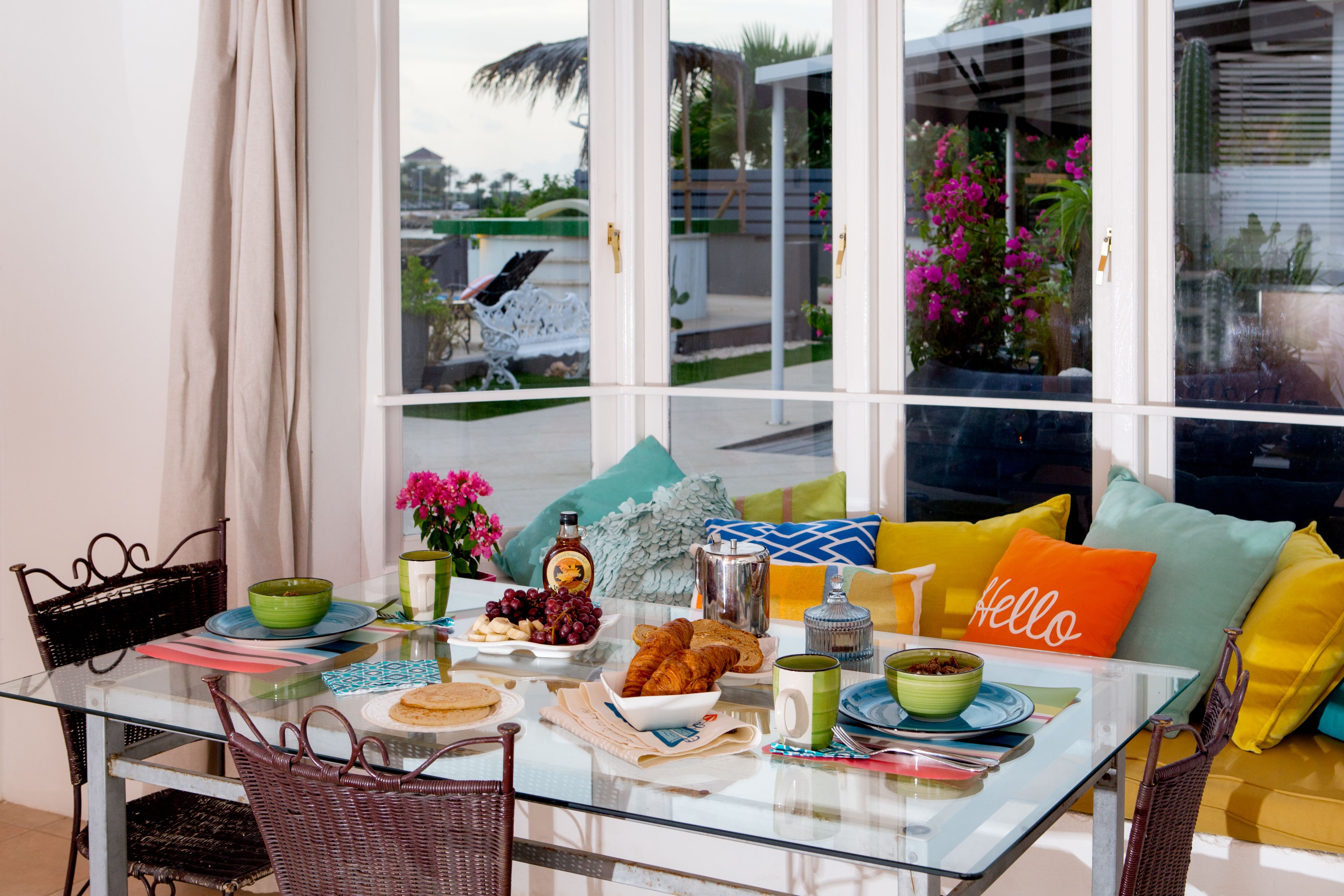 Una mesa de desayuno con diversas opciones de comida, una silla de mimbre y un sofá con cojines de colores.
