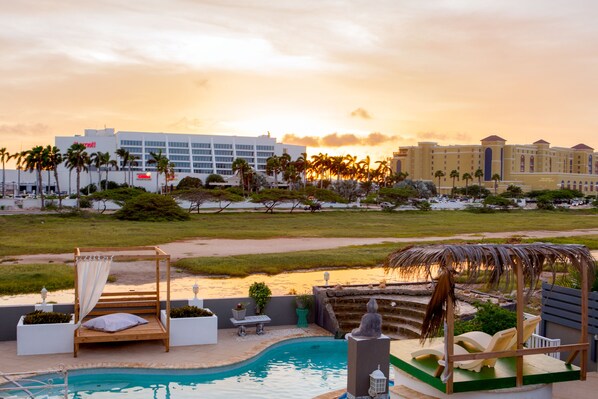 A pool area with a wooden bench, a canopy, and a statue. - Modern Hotel Aruba (Noord)