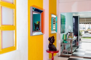 Un pasillo de colores vivos con una escultura sobre una mesa roja, un espejo y vistas al exterior.