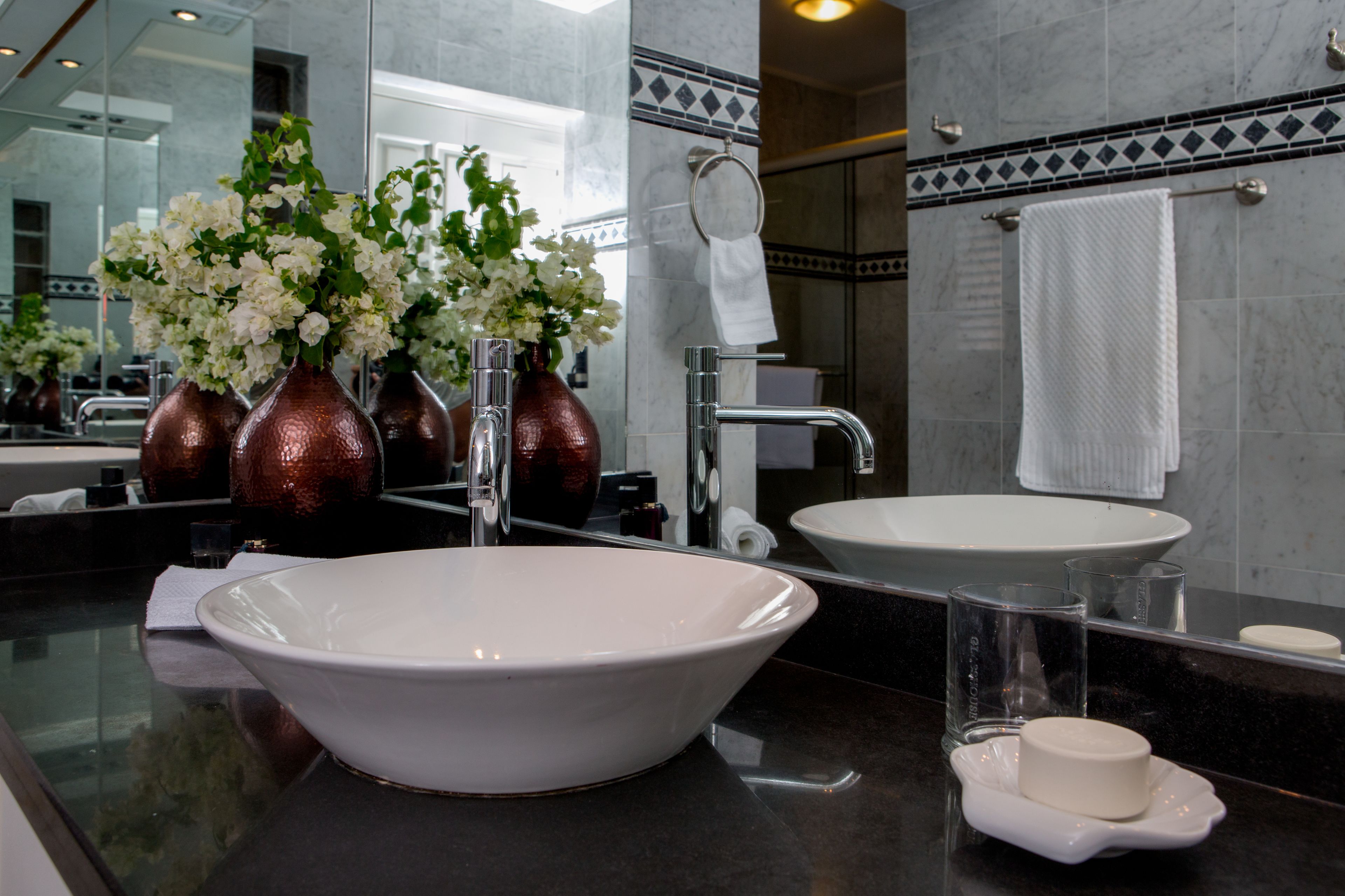 Un baño moderno con un lavamanos grande blanco, un espejo y un florero con flores blancas.