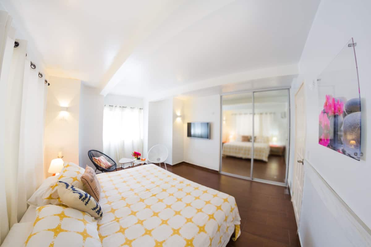 A hotel room with a bed, a chair, a desk, a TV, and a sliding glass door leading to a balcony.