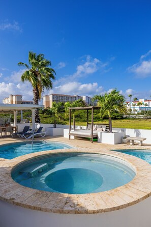 A swimming pool with lounge chairs and a pergola, surrounded by palm trees and a view of a hotel building. - Modern Hotel Aruba (Noord)