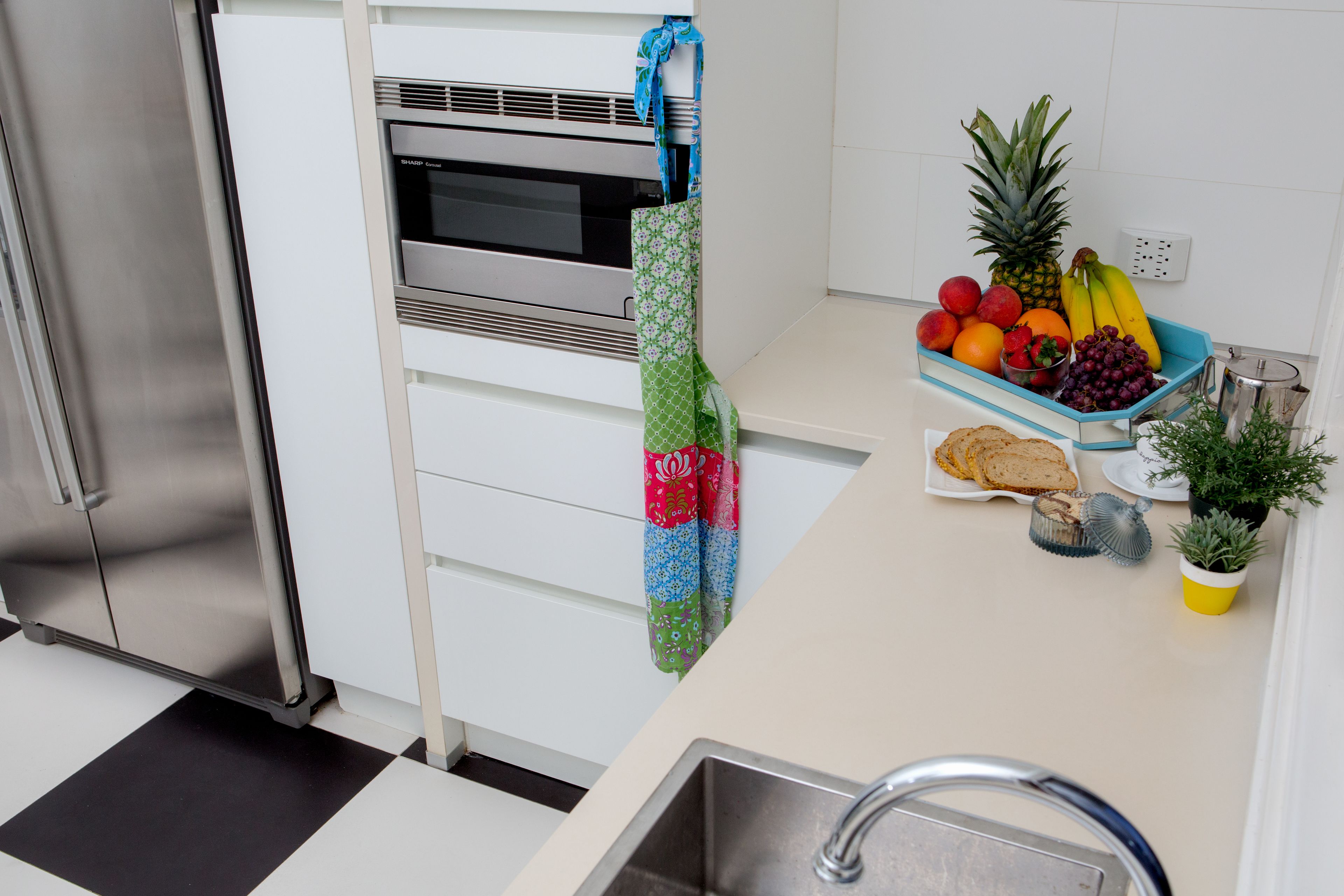 A kitchen with a stainless steel refrigerator, a microwave, a sink, and a fruit bowl with bananas, grapes, and apples.