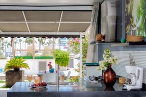 A kitchen with a sink, a coffee maker, and a vase with flowers. There is a plant and a table with chairs outside the window. - Modern Hotel Aruba (Noord)