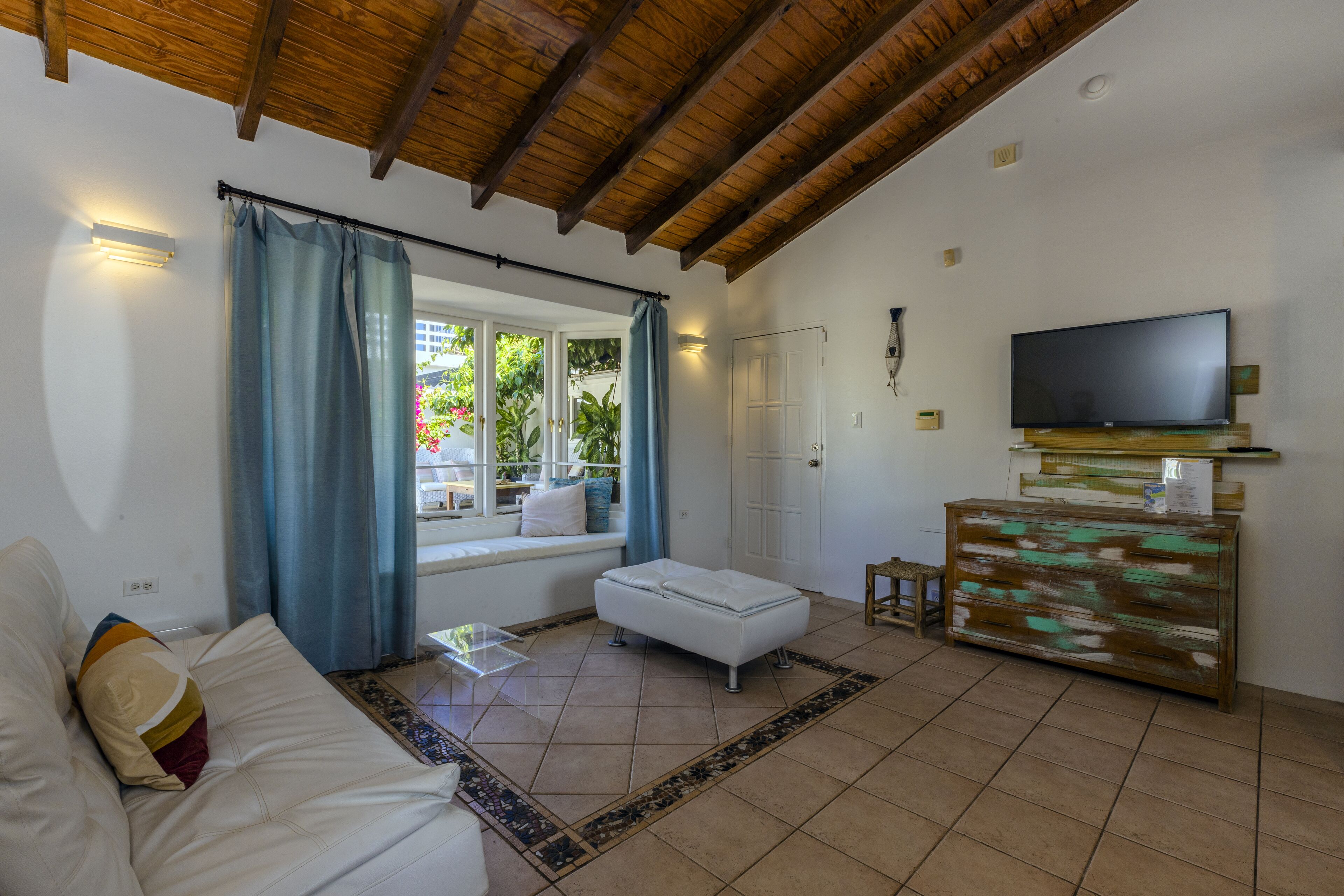 A living room with a white sofa, a small ottoman, a wooden cabinet, and a flat-screen TV.