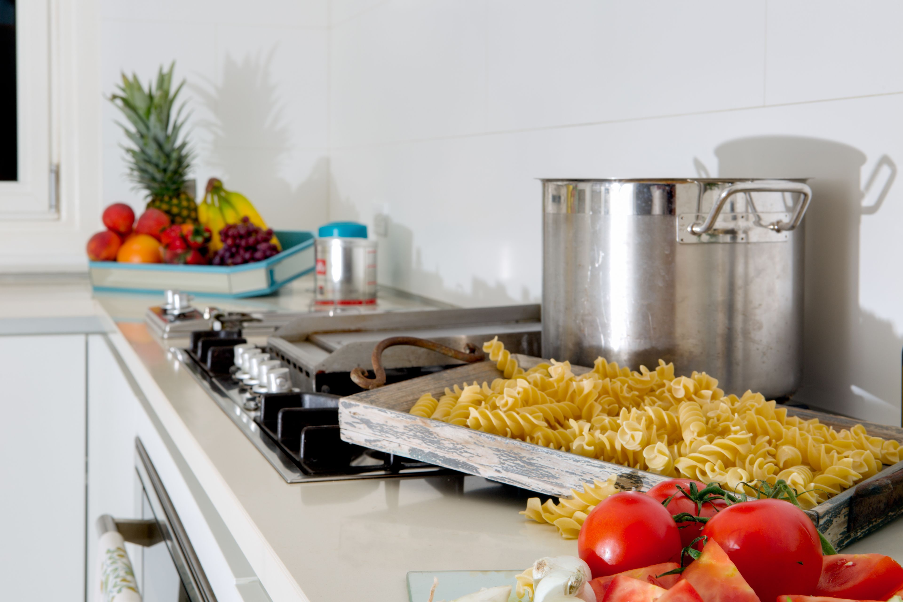 A kitchen counter with pasta, tomatoes, and a pot.
