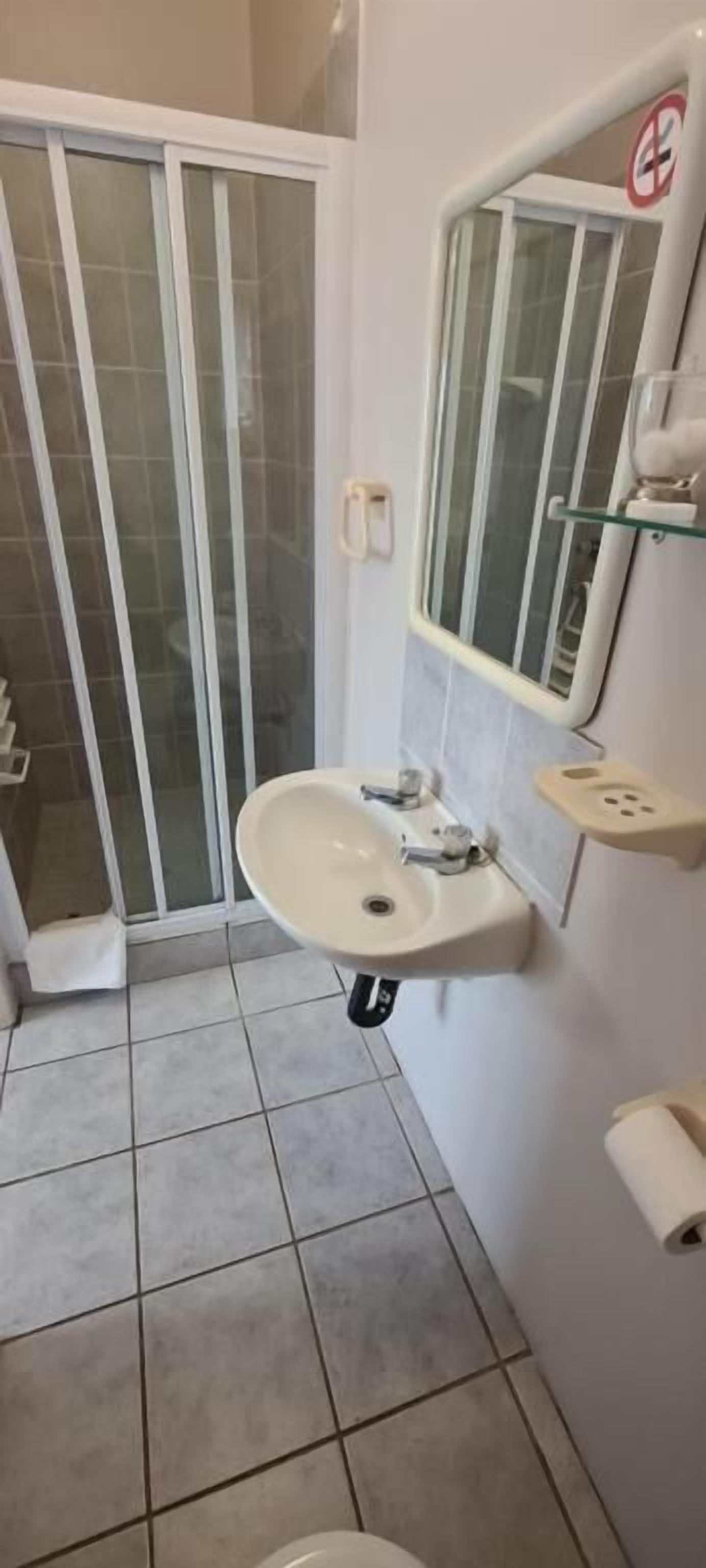 Casa de banho com lavatório, espelho e chuveiro.