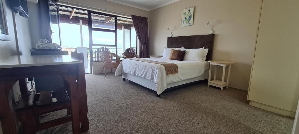 A hotel room with a bed, a desk, a chair, and a view through a large window.