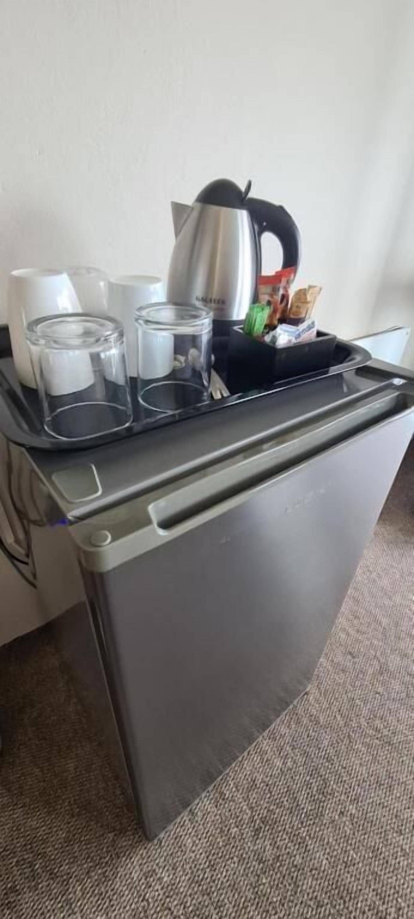 A compact kitchenette with a kettle, cups, and a tray with utensils.