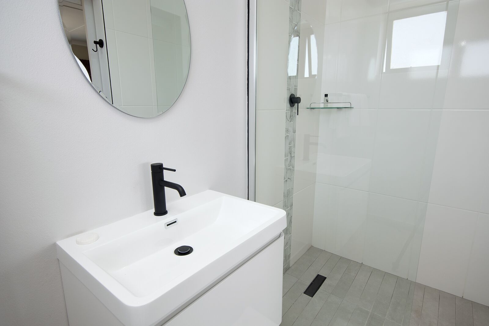 A modern bathroom with a white sink, black faucet, and a glass shower enclosure.