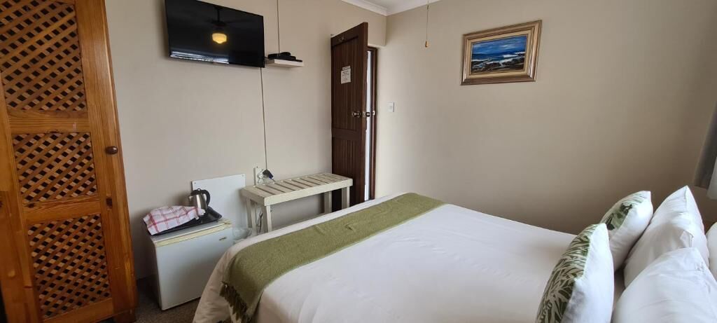 Ein Hotelzimmer mit Bett, einem kleinen Tisch mit Wasserkocher, einem an der Wand montierten Fernseher und einer Tür.